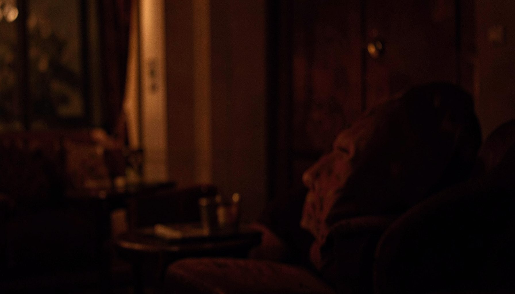 Dimly lit interior scene with warm amber and deep crimson tones, soft ambient glow suggesting an intimate viewing atmosphere
